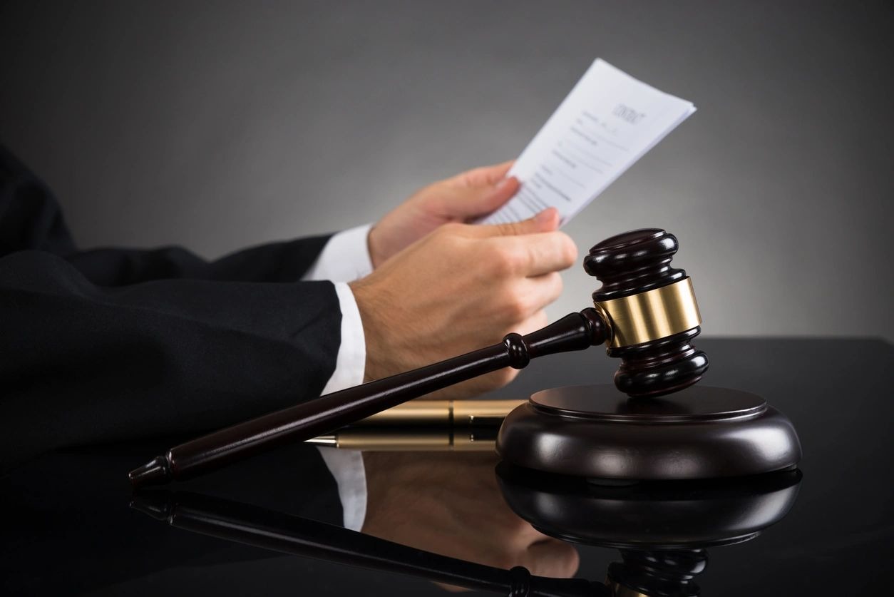 Close-up Of Judge Holding Document With Gavel At Desk